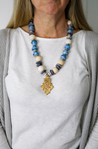 Chunky statement necklace in beautiful blue tones made with sustainable recycled paper beads, featuring a unique brass Ethiopian coptic cross pendant.