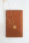 Brown leather passport cover and gold necklace that says "Be the light"
