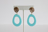 Pair of modern aqua blue resin dangle earrings with textured gold studs on display.