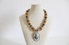 Necklace with wooden beads and a silver pendant on a mannequin bust against a white background.