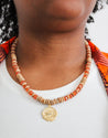 orange beaded with wood necklace with a big, gold charm.