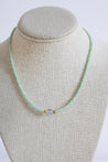 green and white small beaded necklace with a clear bead in the middle with gold bead accents in each side.
